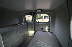 Innenansicht eines ausgestatteten Microcampers Nissan NV 200 mit Küchenblock, ausziehbarer Sitzbank / Schlafbank, Fußboden und Wandverkleidung.